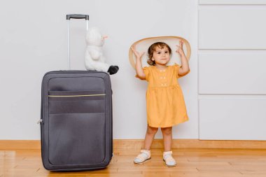 Büyük bir bavulun yanında beyaz şapkalı küçük bir kız pelüş kardan adam oyuncağıyla oynuyor. Çocuklar tatil danışmanlığı istiyor.