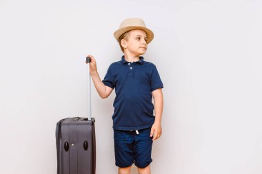 Mutlu çocuk beyaz arka planda büyük bir bavul taşıyor ve büyük bir tatil bekliyor.