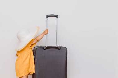 Büyük bir bavulun yanında beyaz şapkalı küçük bir kızın arka görüntüsü. Çocuklar bir tatil konsepti istiyor. Beyaz arkaplan kopyalama alanı