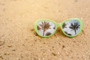 Kumun üzerindeki güneş gözlüğünü palmiyelerin yansımasıyla kapat. Tatil kavramı