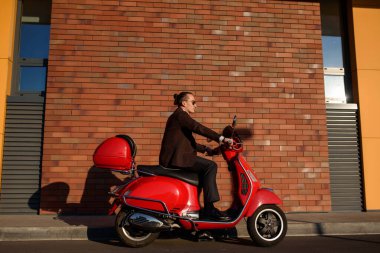 Klasik takım elbiseli, kırmızı motosikletli, zarif bir adamın sokak fotoğrafı konsepti. Tuğlalardan arkaplan duvarı