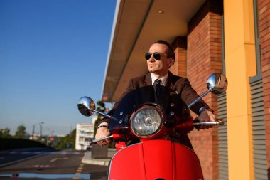 Gün batımında kırmızı bir scooter kullanan zarif bir adamın sokak fotoğrafı.