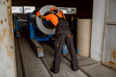 Metal bir bobini iten ve metal kiremit çatı işlemine hazırlayan işçilerin arka planı. Endüstri kavramı.