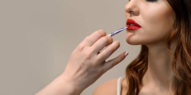 Genç bir kadının yakın portresi. Makyöz eli, genç bir kadının dudaklarına fırçayla kırmızı ruj sürüyor. Metin için boşluk kopyala