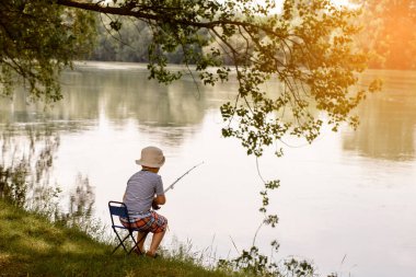 Yaz tatili konsepti. Şapkalı küçük çocuk gölde balık tutuyor.