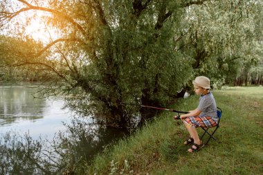 Yaz tatili konsepti. Şapkalı küçük çocuk gölde balık tutuyor.