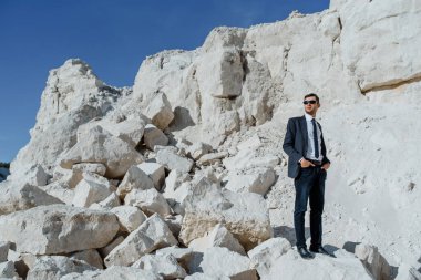 Klasik kıyafetler, ceket, kravat ve gözlüklü genç adam dağda poz veriyor.. 