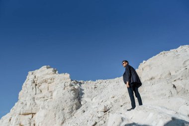 Klasik kıyafetler, ceket, kravat ve gözlüklü genç adam dağda poz veriyor.. 