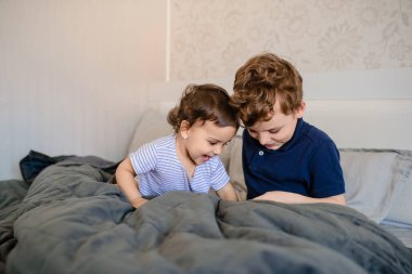 Mutlu erkek ve kız kardeşler gülümsüyor, gülüyor, yatakta uzanıyor, akıllı telefonda oynuyor ve eğleniyorlar.