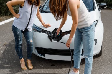 Güç kablosu tutan ellerini kapat ve elektrikli arabanın aküsünü şarj et. Çevre dostu araba, şarj istasyonunda elektrikli araba aküsü şarj ediliyor. Çevre taşımacılığı kavramı