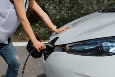 Güç kablosu tutan ellerini kapat ve elektrikli arabanın aküsünü şarj et. Çevre dostu araba, şarj istasyonunda elektrikli araba aküsü şarj ediliyor. Çevre taşımacılığı kavramı
