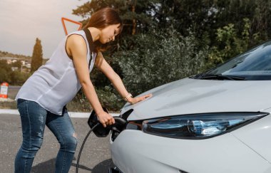 Genç ve güzel bir kadın ormanda bulunan şarj istasyonunda elektrikli arabasını şarj ediyor. Çevre dostu trasport cocnept