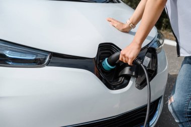 Güç kablosu tutan ellerini kapat ve elektrikli arabanın aküsünü şarj et. Çevre dostu araba, şarj istasyonunda elektrikli araba aküsü şarj ediliyor. Çevre taşımacılığı kavramı