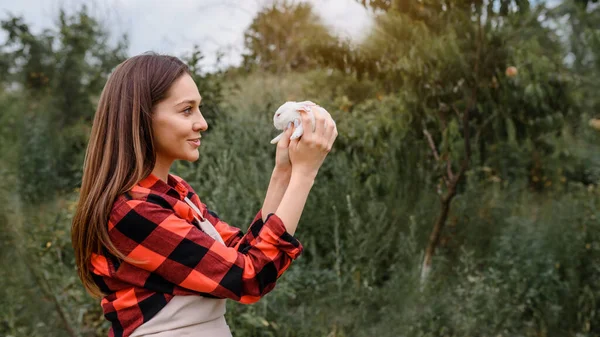 Νεαρή Χαρούμενη Χαμογελαστή Αγρότισσα Κρατάει Ένα Λευκό Κουνελάκι Στα Χέρια — Φωτογραφία Αρχείου