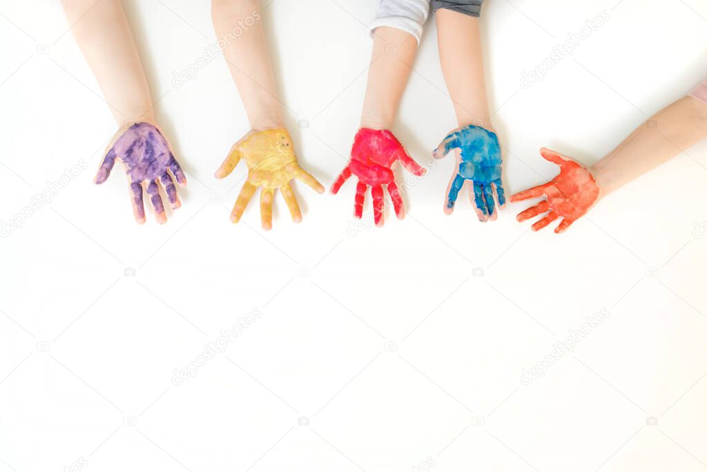 Close children's hands painted with yellow, blue pink, purple and orange paint gouache with on white background. Free space for text copy space