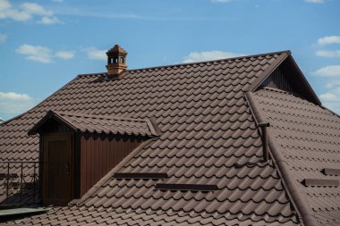 Mavi gökyüzünde bulutlu bir evin kahverengi çatısı. 