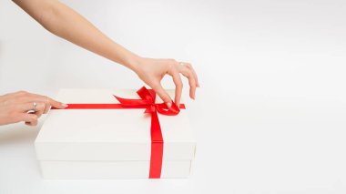 Female hands holding a gift box white with a red ribbon, one object on a white background. Gift holiday. Festive background. Top View. Free space for text