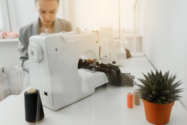 Picture of young woman tailor working on a sewing machine with sun reflection. Picture shot through the glass