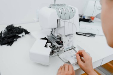 Interior of overlock machine/ serger concept. Female tailor is introducing thread to overlock machine/ serger on the table in her mini tailoring workshop.