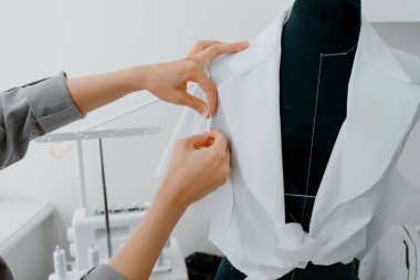 Close up of young woman tailor is arranging a future shirt on a mannequin in her mini workshop. On the table are: overlock  and sewing machine. Creative design concept.