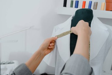 Young woman tailor is measuring with a centimeter ribbon a future shirt on a mannequin in her mini workshop