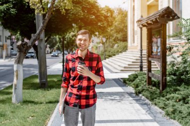 Genç, mutlu, serbest çalışan bir adam sokakta elinde bir kahve ve dizüstü bilgisayarla yürüyor. Her yerde çalışma kavramı
