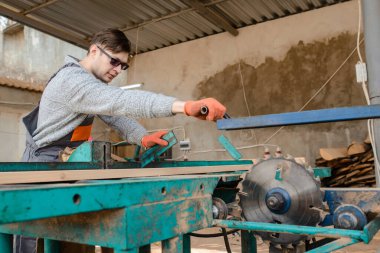 Ahşap kereste deposundaki genç marangoz tahta / tahta kesiyor.