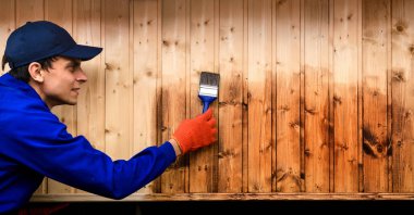 İnşaat alanındaki tahtalardan ahşap duvar fırçasıyla boyanmış genç bir müteahhit. Çit için vernik uyguluyor. Cilalama işlemi. Metin için boşluk kopyala