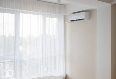 Dairenin beyaz iç kısmı. Büyük bir pencerenin yanında bir klima, parlak bir oda