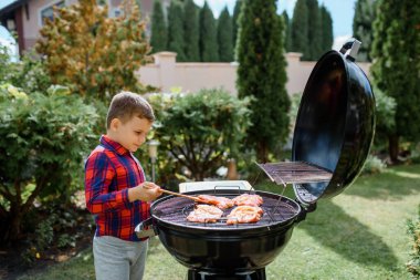 Genç çocuk evin bahçesindeki ızgarada barbekü hazırlıyor.