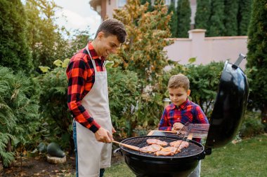 Genç baba ve oğlu evlerinin arka bahçesindeki bir ızgarada barbekü pişiriyor ve eğleniyorlar. Mutlu aile kavramı