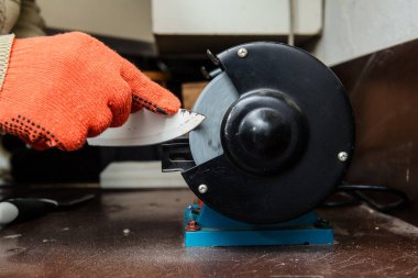 Kapalı bıçak bileyicisi, koruyucu eldivenli bir işçi dairesel testereyle bıçağı biliyor.