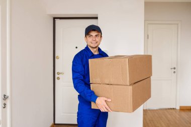 Mavi üniformalı genç teslimatçı beyaz odadaki müşteri için bir paket yolluyor..