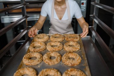 Yakın çekim yapan fırıncı, fırın fabrikasında taze simit dolu bir tepsi tutuyor. Lezzetli fırın fabrikası konsepti..