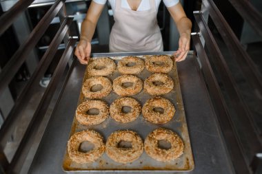 Yakın çekim yapan fırıncı, fırın fabrikasında taze simit dolu bir tepsi tutuyor. Lezzetli fırın fabrikası konsepti..