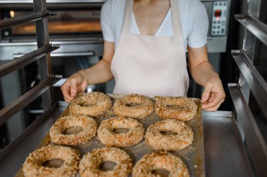 Yakın çekim yapan fırıncı, fırın fabrikasında taze simit dolu bir tepsi tutuyor. Lezzetli fırın fabrikası konsepti..