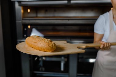 Kafkasyalı genç fırıncının yakınında fırının yanında taze ekmek ve ahşap kabuğu olan bir fırın var. Lezzetli ekmek fırını konsepti.