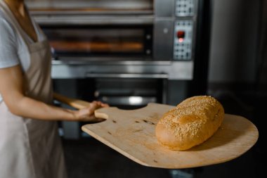 Kafkasyalı genç fırıncının yakınında fırının yanında taze ekmek ve ahşap kabuğu olan bir fırın var. Lezzetli ekmek fırını konsepti.