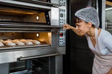 Kafkasyalı genç fırıncı bir fırının elektrikli fırınında ekmek pişirme sürecine bakıyor. Fransız ekmeği fırını konsepti. 