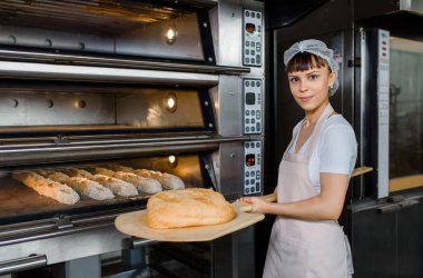 Kafkasyalı genç fırıncı fırının yanında taze ekmek ve ahşap kabuğu tutuyor. Lezzetli ekmek fırını konsepti.