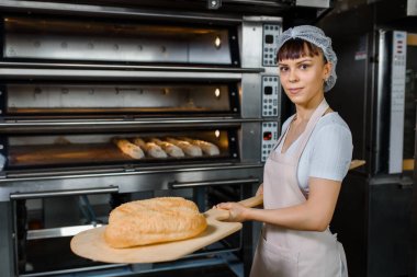 Kafkasyalı genç fırıncı fırının yanında taze ekmek ve ahşap kabuğu tutuyor. Lezzetli ekmek fırını konsepti.
