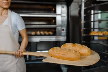 Kafkasyalı genç fırıncının yakınında fırının yanında taze ekmek ve ahşap kabuğu olan bir fırın var. Lezzetli ekmek fırını konsepti.