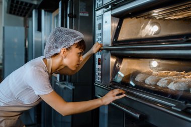 Kafkasyalı genç fırıncı bir fırının elektrikli fırınında ekmek pişirme sürecine bakıyor. Fransız ekmeği fırını konsepti. 