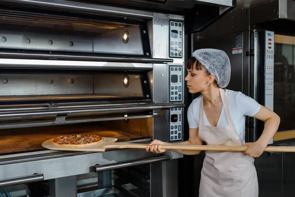 Młoda Biała Kobieta Piekarz Trzyma Skórkę Drewna Świeżą Pizzą Wkłada — Zdjęcie stockowe