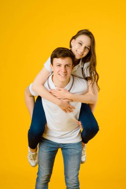 Beyaz tişörtlü mutlu bir çiftin portresi. Sarı arka planda gülüyor ve gülümsüyor.