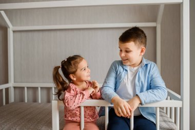 İki çocuk erkek ve kız kardeş Montessori yatağında oturmuş birbirlerine bakıyorlar. Ev şeklindeki çocuklar için yatak
