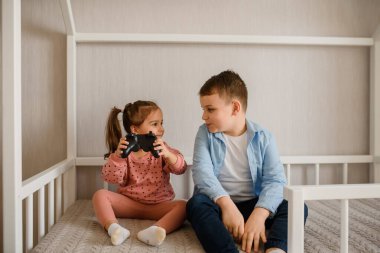İki çocuk erkek ve kız kardeş Montessori yatağında oturmuş oyun oynuyorlar. Kız bir oyun sahası tutuyor ve oğlan ona bakıyor.