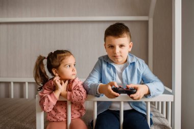 İki çocuk erkek ve kız kardeş Montessori yatağında oturmuş oyun oynuyorlar. Oğlan bir av alanı tutuyor ve kız ona bakıyor..