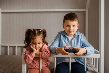 İki çocuk erkek ve kız kardeş Montessori yatağında oturmuş oyun oynuyorlar. Oğlan bir av alanı tutuyor ve kız ona bakıyor..
