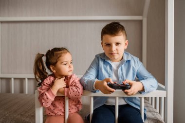 İki çocuk erkek ve kız kardeş Montessori yatağında oturmuş oyun oynuyorlar. Oğlan bir av alanı tutuyor ve kız ona bakıyor..